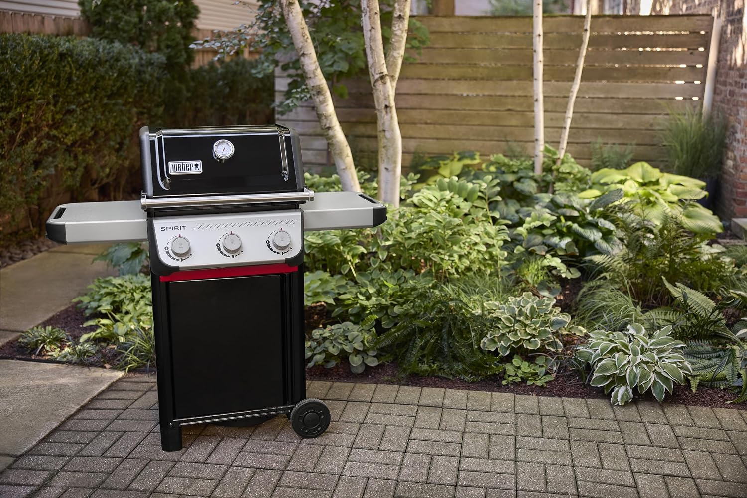 Barbecue à gaz Weber Spirit E-310 en fonctionnement dans un jardin l'été